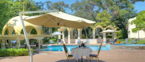 A poolside area with a table and chairs, umbrellas, and a pool.