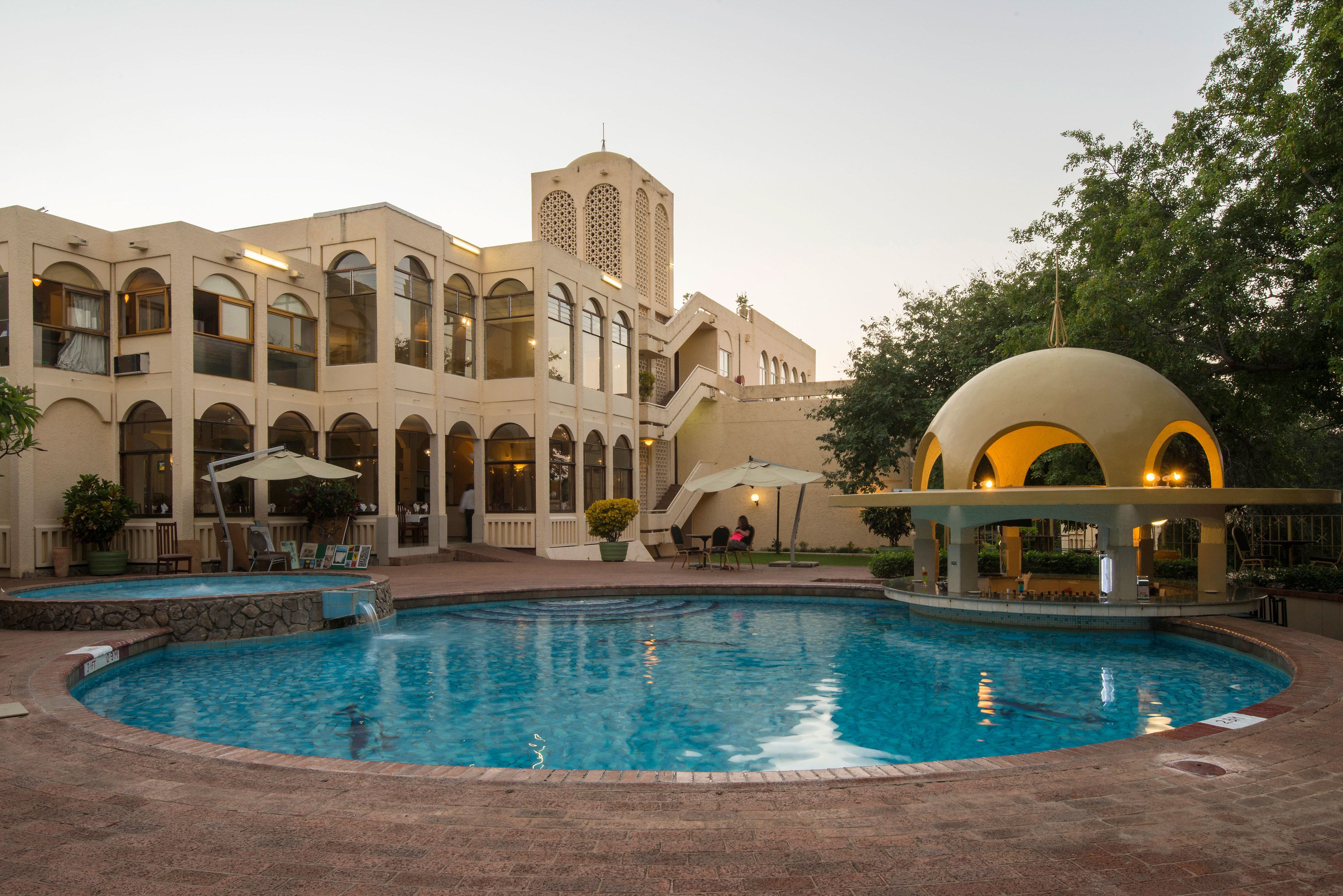 Zona de piscina con un edificio que tiene ventanas arqueadas y una torre.