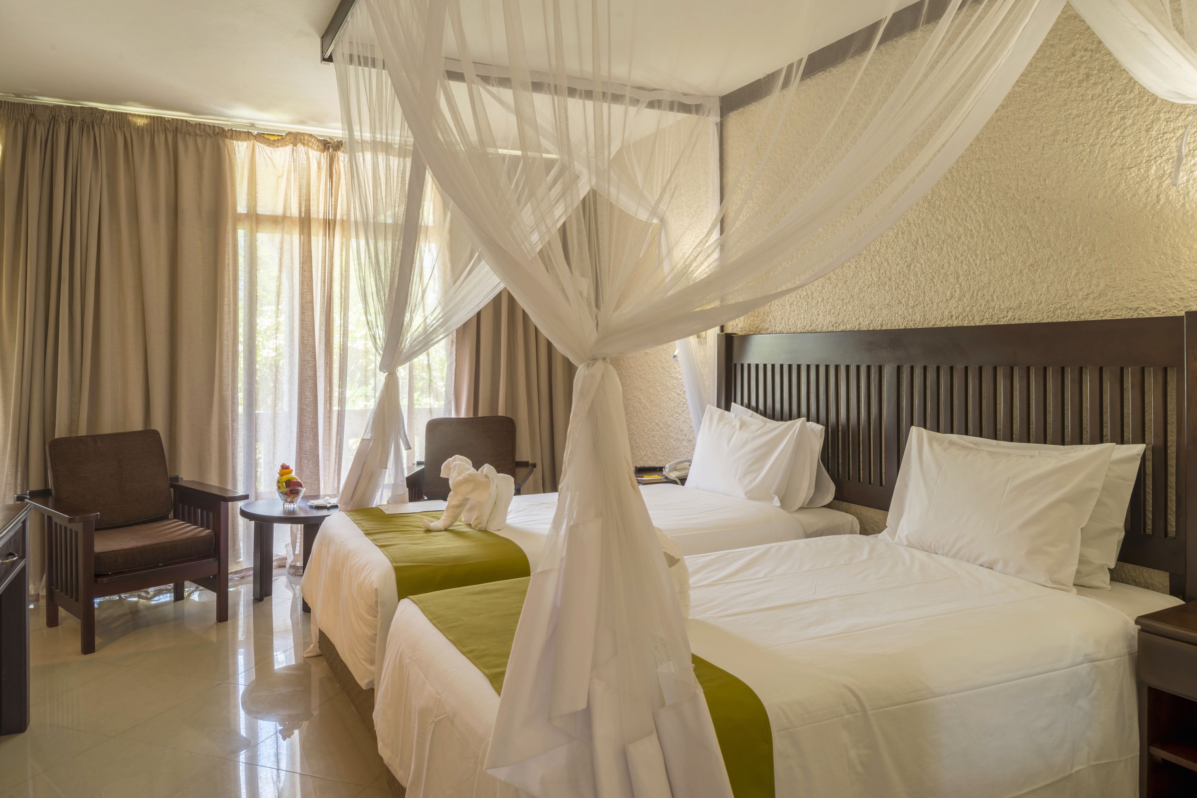 A hotel room with two beds, a sitting area with a chair and a table, and a canopy bed with a white canopy.