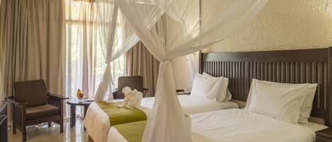 A hotel room with two beds, a sitting area with a chair and a table, and a canopy bed with a white canopy.