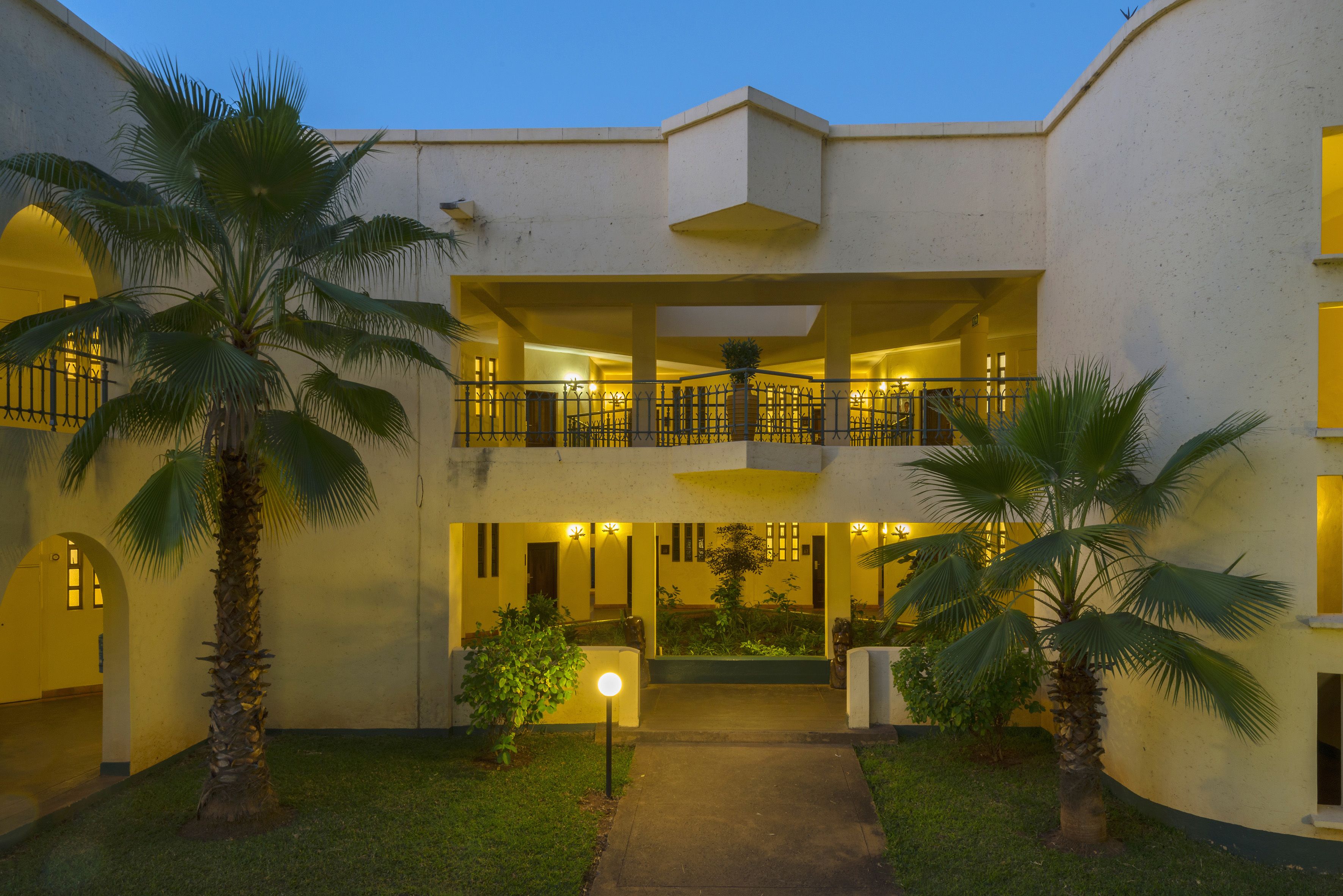 A two-story building with a central courtyard, featuring palm trees and a well-lit entrance.
