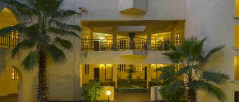 A two-story building with a central courtyard, featuring palm trees and a well-lit entrance.