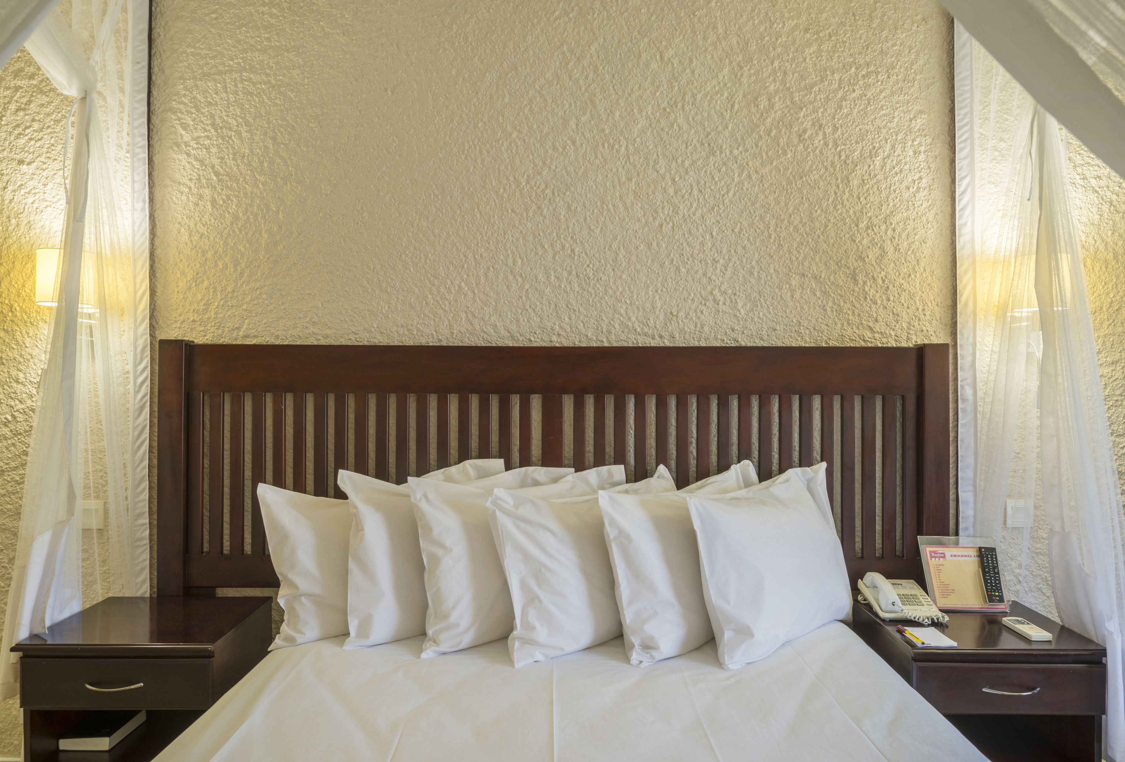 A hotel room with a large bed, white bedding, a wooden headboard, a bedside table with a lamp, and a phone.