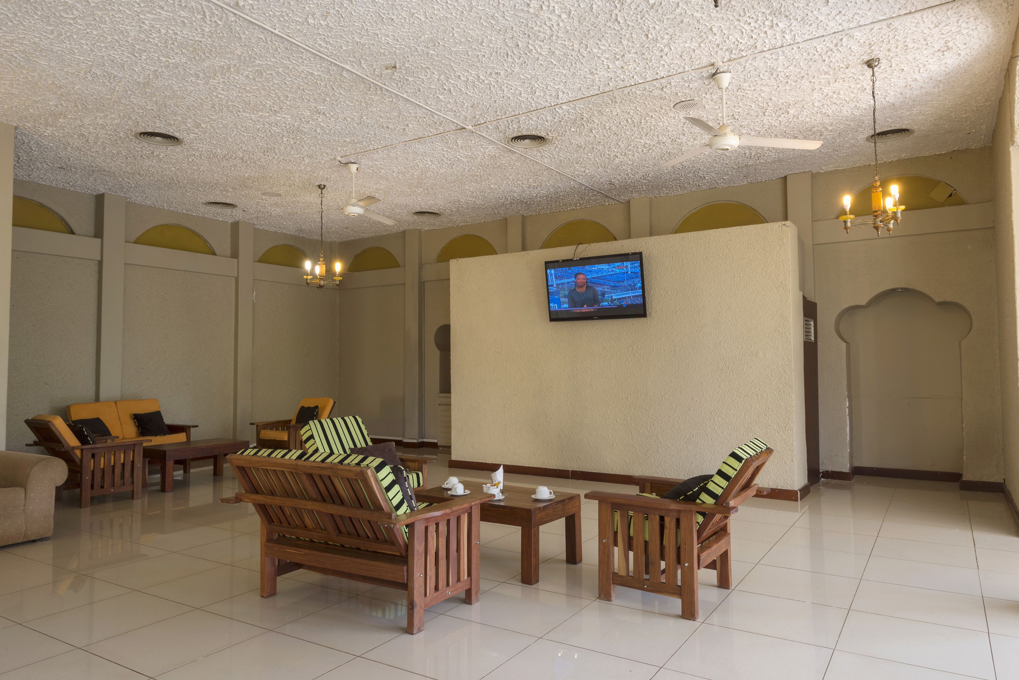 A spacious lobby with wooden furniture, a flat-screen TV mounted on the wall, and a ceiling fan.