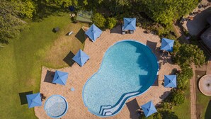 Luftaufnahme eines Poolbereichs mit mehreren Sonnenschirmen, Liegestühlen und einer kleinen, runden Wasserspiels.