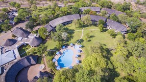 Ein Luftbild eines Resorts mit strohgedeckten Gebäuden, einem Schwimmbad und umgebender Bepflanzung.