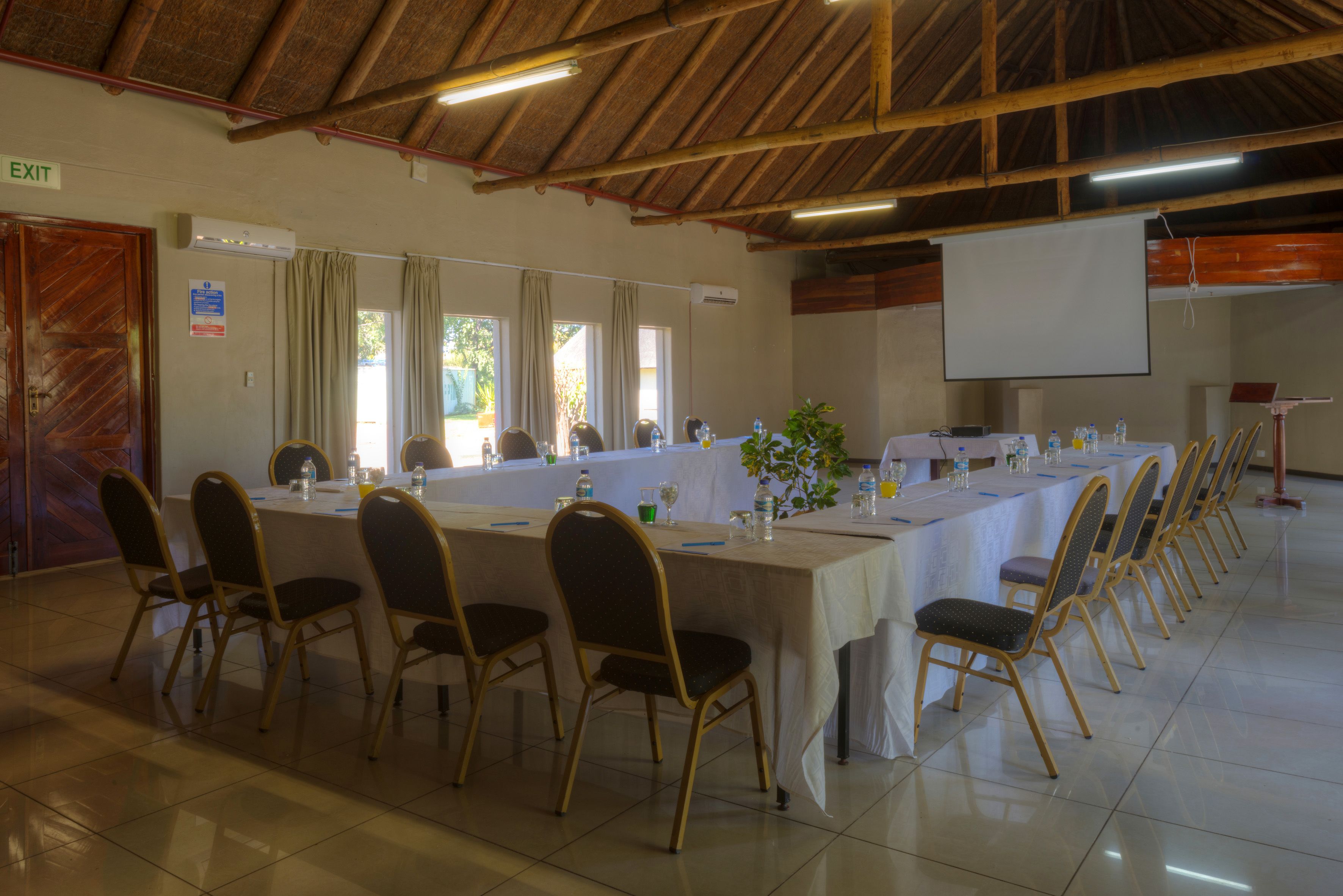 A conference room with a long table, chairs, a projector screen, and an exit sign.