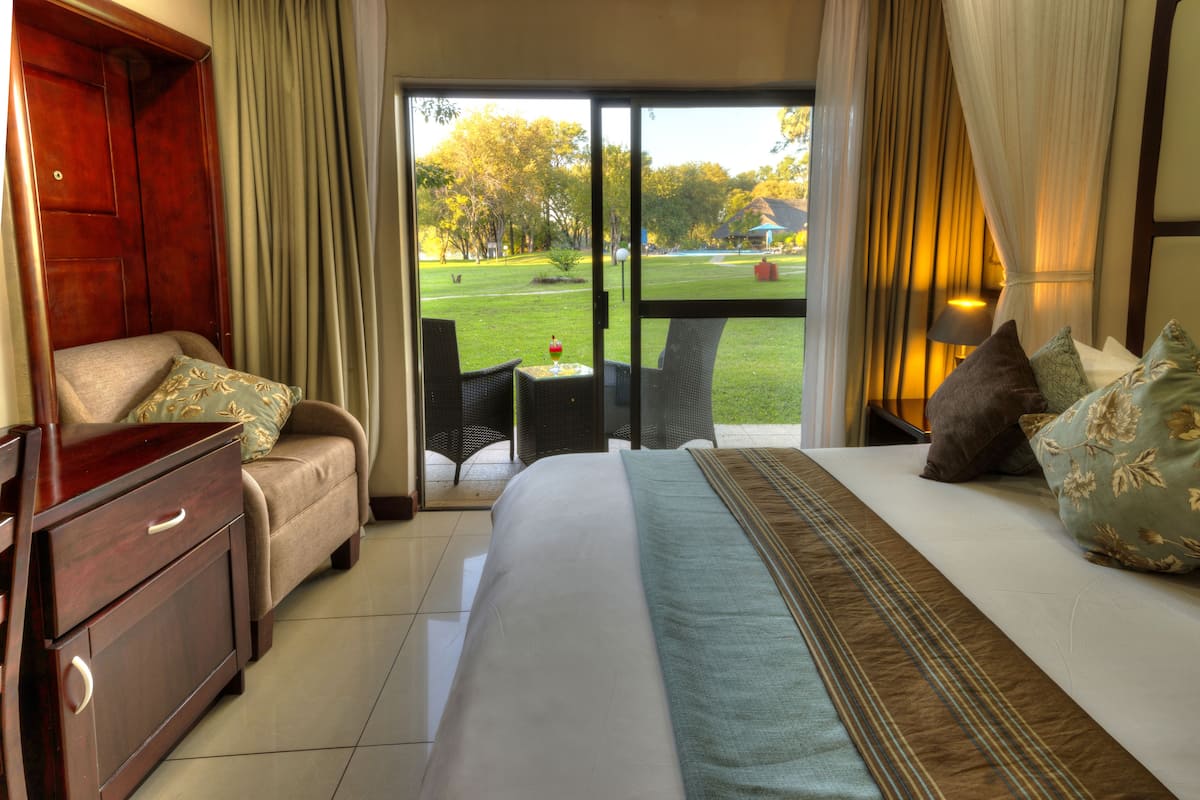 Ein Hotelzimmer mit Bett, Schreibtisch, Stuhl und Blick auf einen Garten durch das Fenster.
