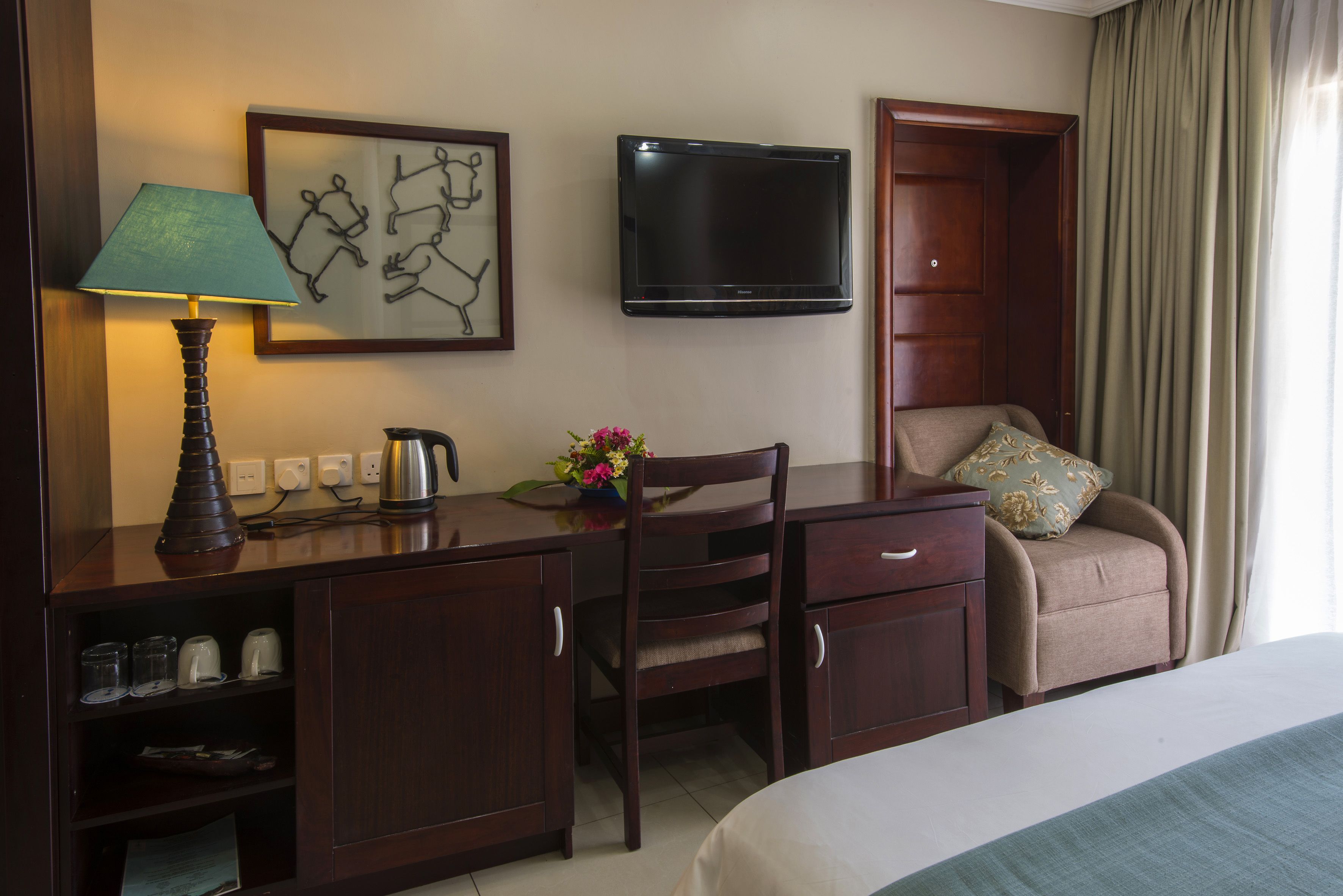 Ein Hotelzimmer mit einem Bett, einem Schreibtisch mit Lampe, einem Sessel, einem Fernseher und einer Kaffeemaschine.