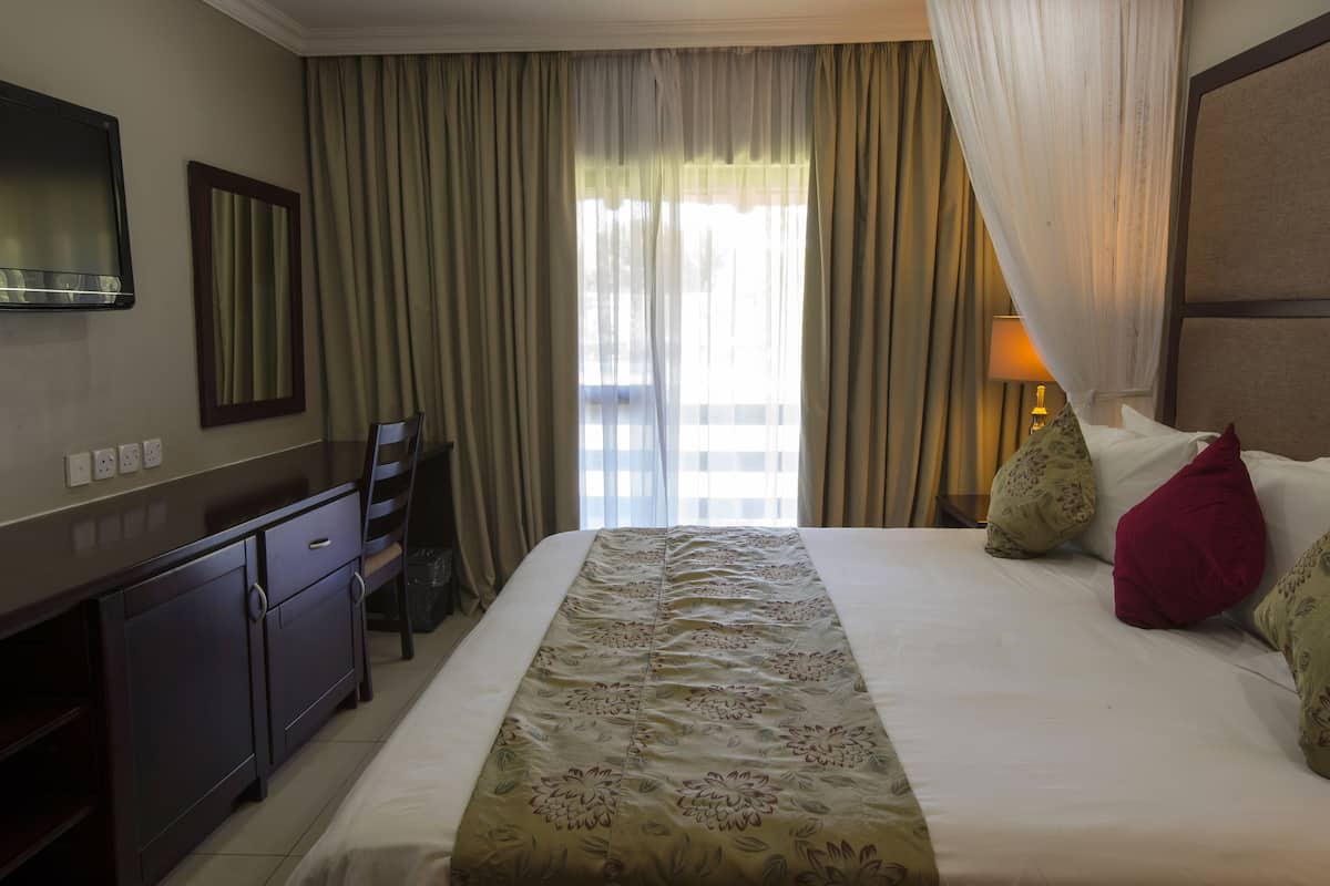 Ein Hotelzimmer mit Bett, Schreibtisch, Stuhl, Fernseher und Vorhängen.