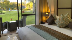 Ein Hotelzimmer mit großem Fenster, einem Bett mit gestreifter Decke, einem Nachttisch mit Lampe und Blick auf einen Golfplatz.