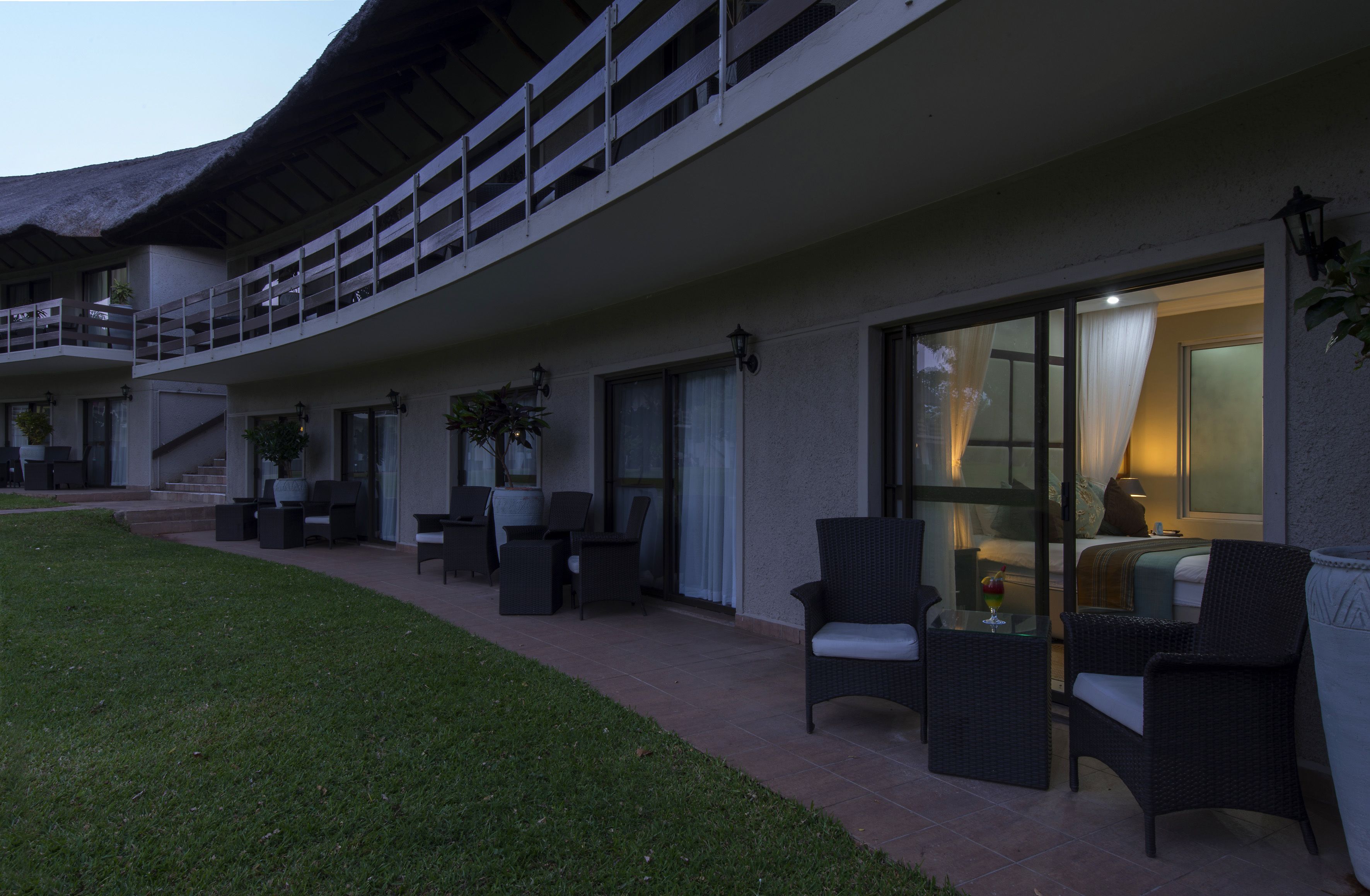 A hotel with a covered outdoor seating area, a staircase, and a room with a bed and a lamp.