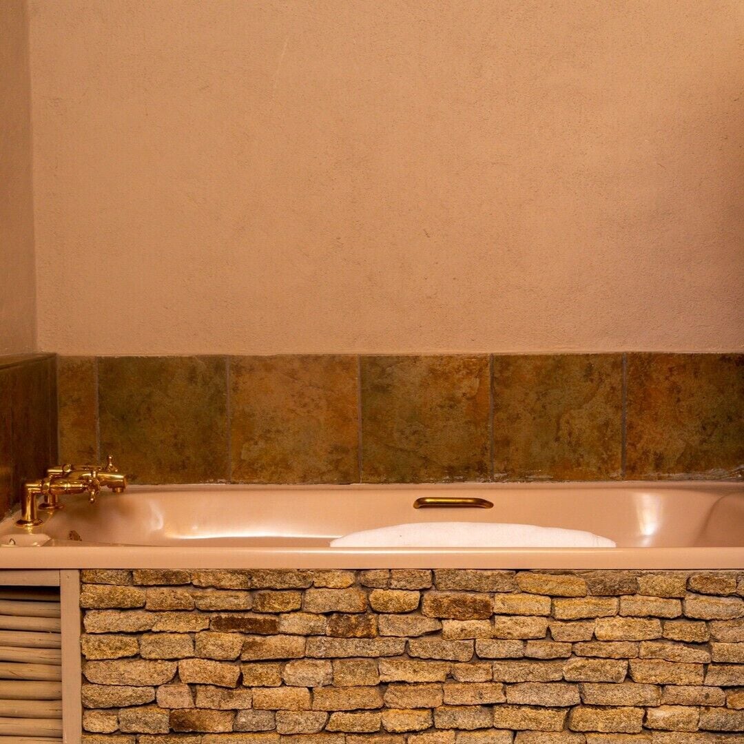 A bathroom with a stone wall, a bathtub, and a gold faucet.