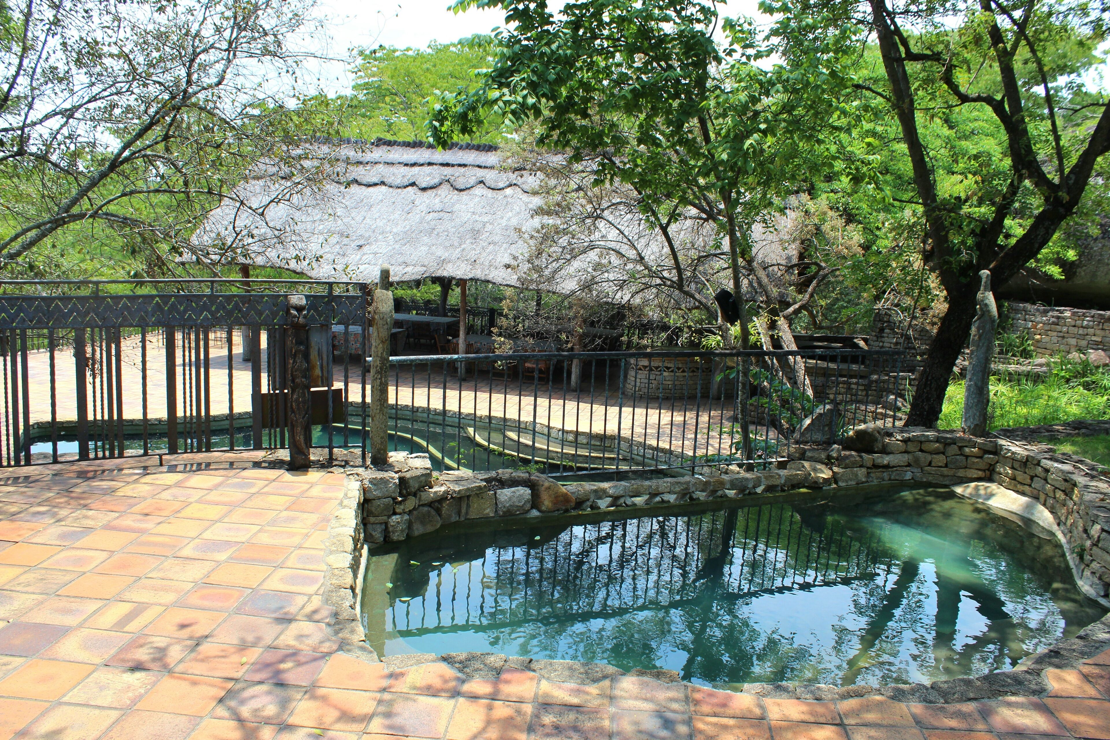 A courtyard with a stone pool, a tiled floor, and a thatched-roof structure.
