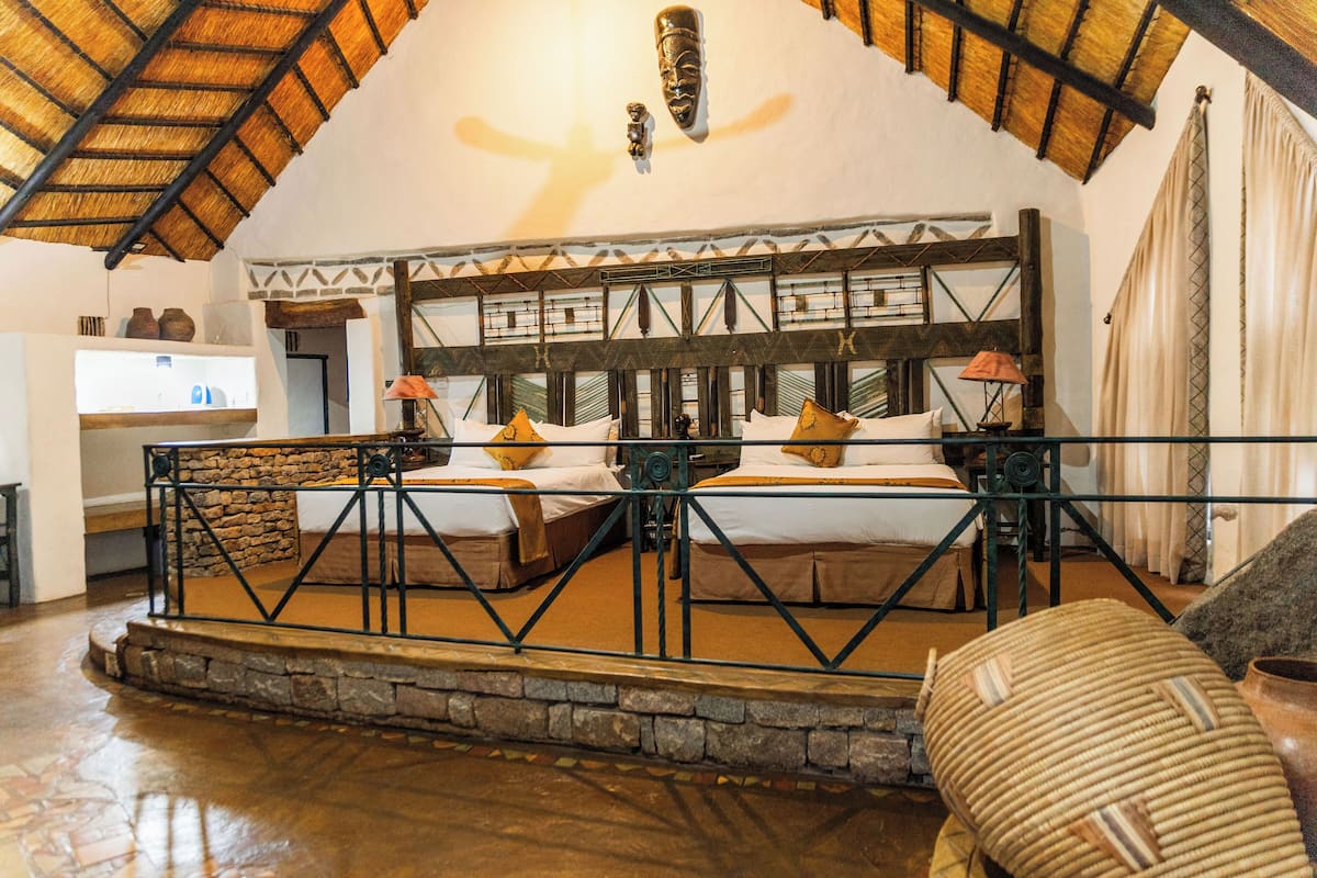 Una habitación con techo alto, techo de paja y cama con cabecera de motivos geométricos.