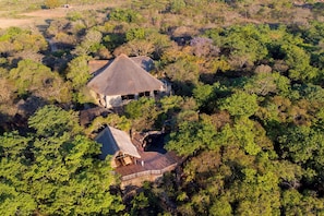 Eine Lodge mit einem Gebäude mit traditionellem Strohdach und einem kleineren Anbau, ebenfalls mit einem Strohdach, umgeben von dichtem Wald.