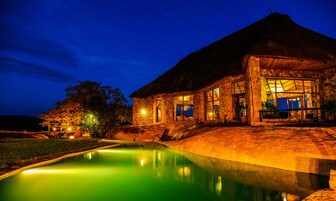 Un edificio de piedra con techo de paja, piscina y un espacio exterior bien iluminado.