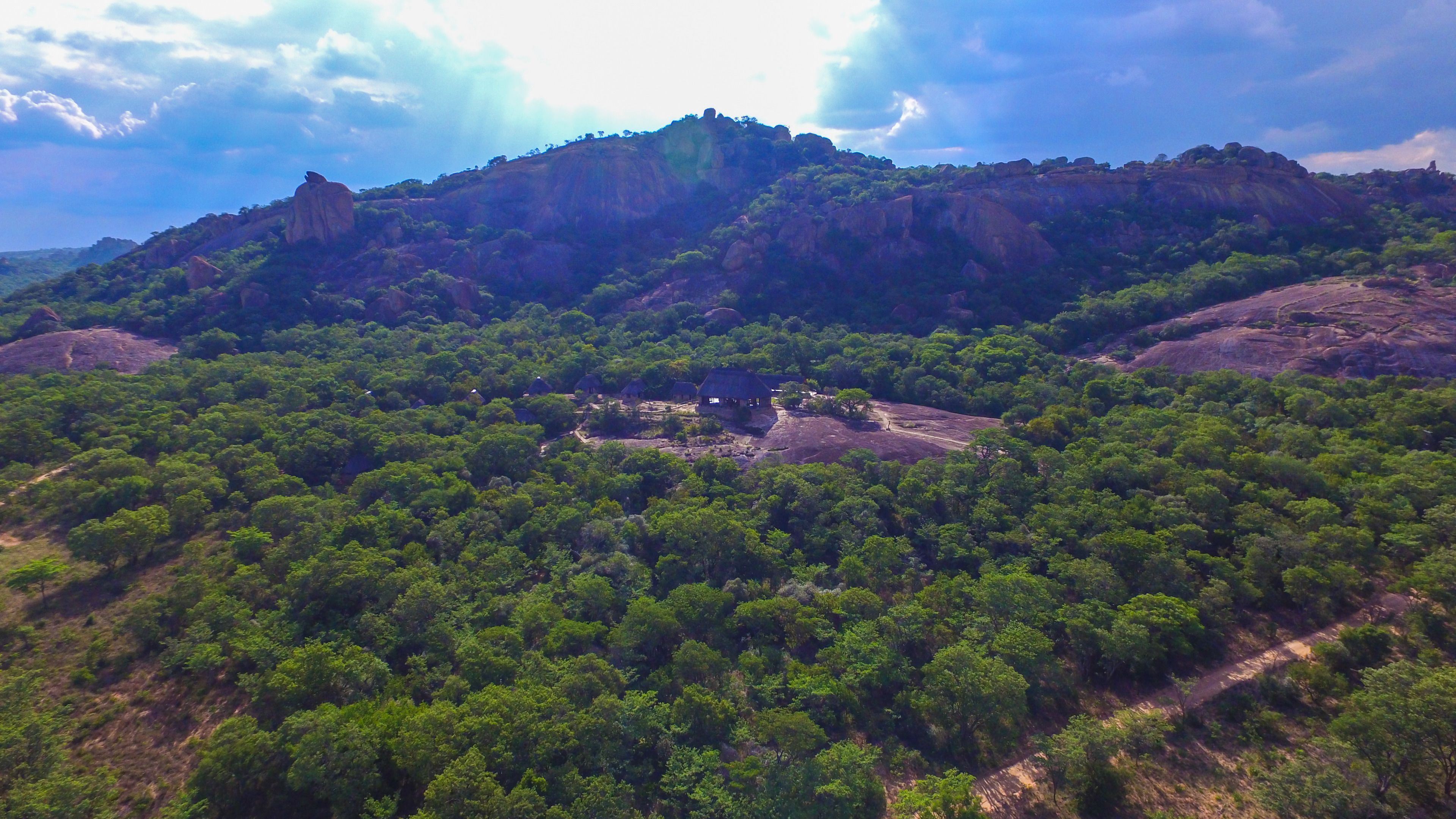 Paisatge de muntanya amb un bosc verd abundant i alguns edificis petits.