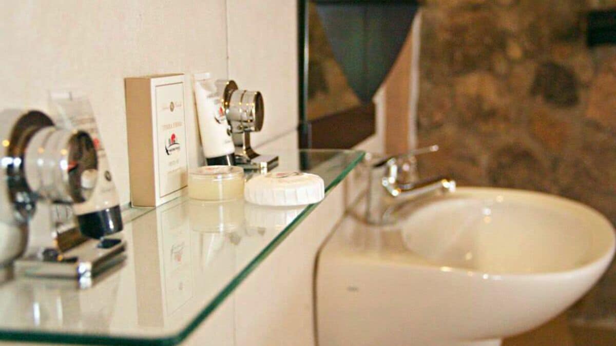 Un baño con encimera de vidrio, lavamanos blanco y artículos de aseo.