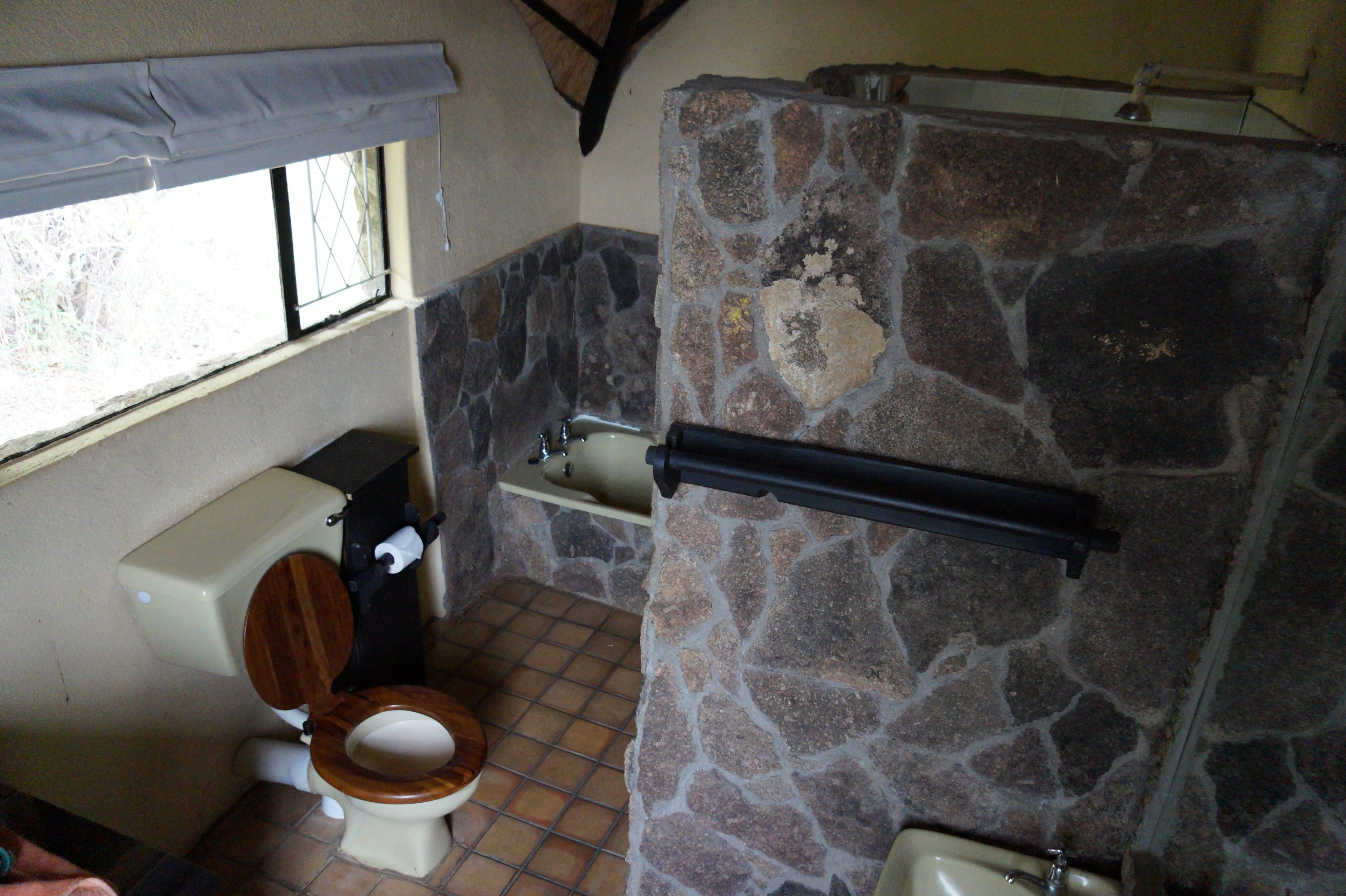 A bathroom with a stone wall, a wooden toilet, and a bathtub.