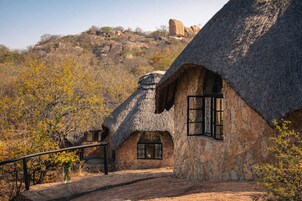 Una casa con techo de paja, paredes de piedra, una escalera de piedra y vistas a un paisaje montañoso.