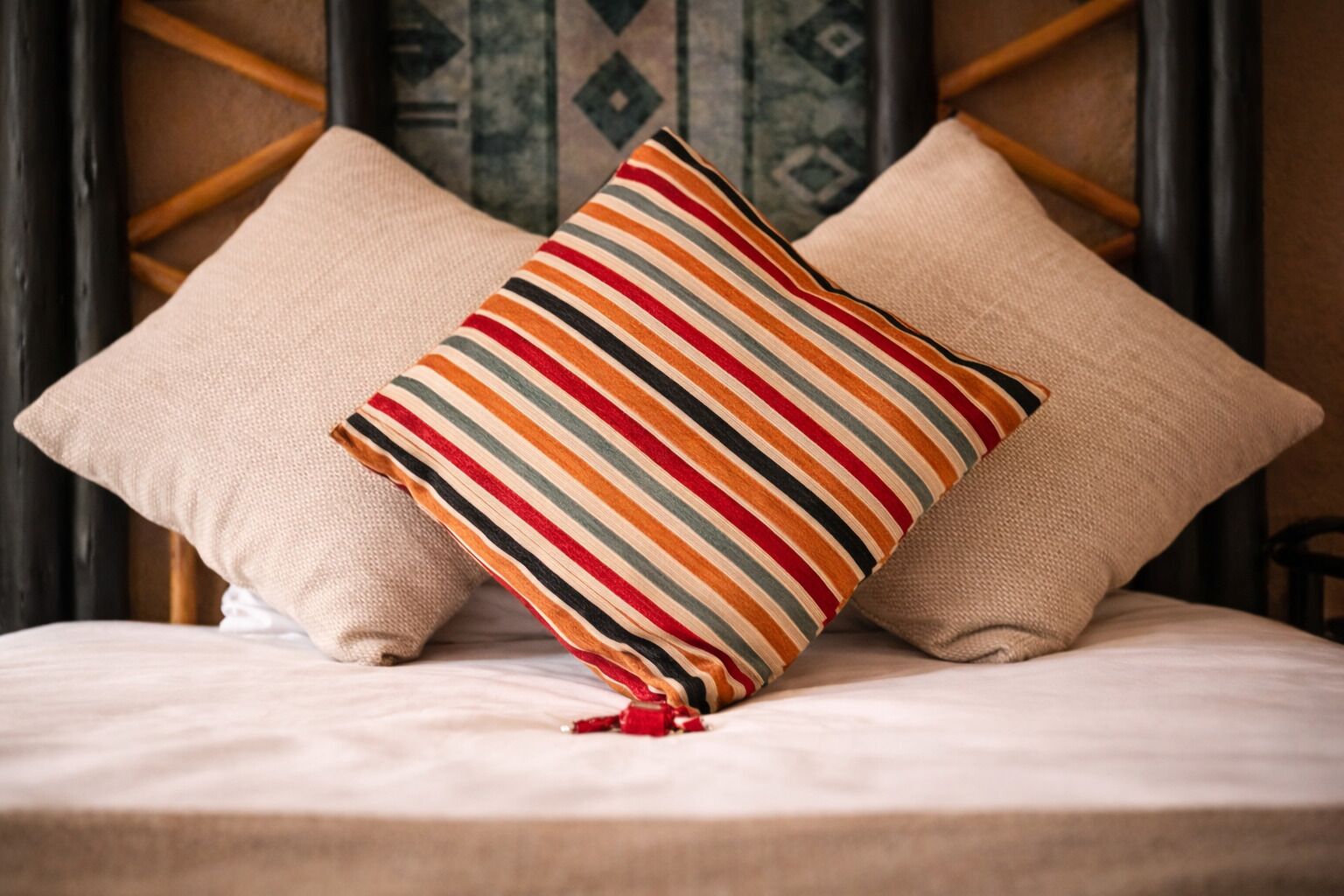 Ein Bett mit zwei beigen Kissen und einem farbenfrohen Kissen mit Streifen.