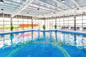 An indoor swimming pool with clear glass walls, benches along the sides, and potted plants. - Foshan Sanshui ShiHuang Garden Hotel (Foshan)