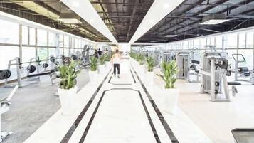 A gym with exercise equipment, a central walkway, and large windows.