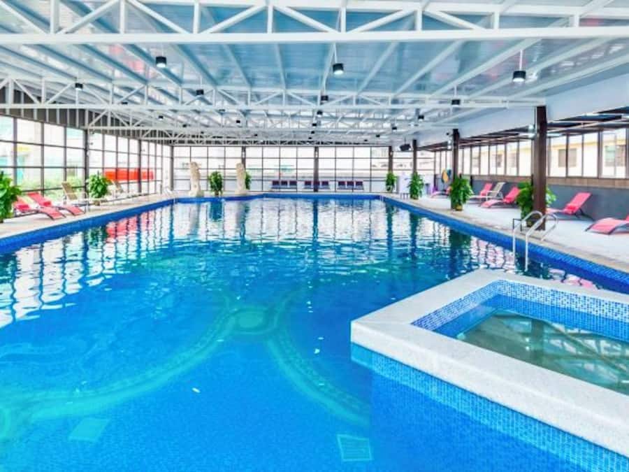 Piscina interna com água azul cristalina, rodeada por espreguiçadeiras e plantas em vasos.