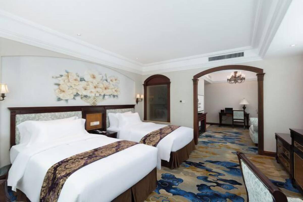 A hotel room with two beds, a floral wall art, a chandelier, and a patterned carpet.