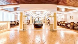 Un hall de hotel espacioso con un mostrador de recepción central, techos altos con paneles de madera y piso de baldosas.