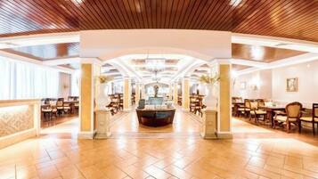 A spacious hotel lobby with a central reception desk, high ceilings with wooden paneling, and a tiled floor.