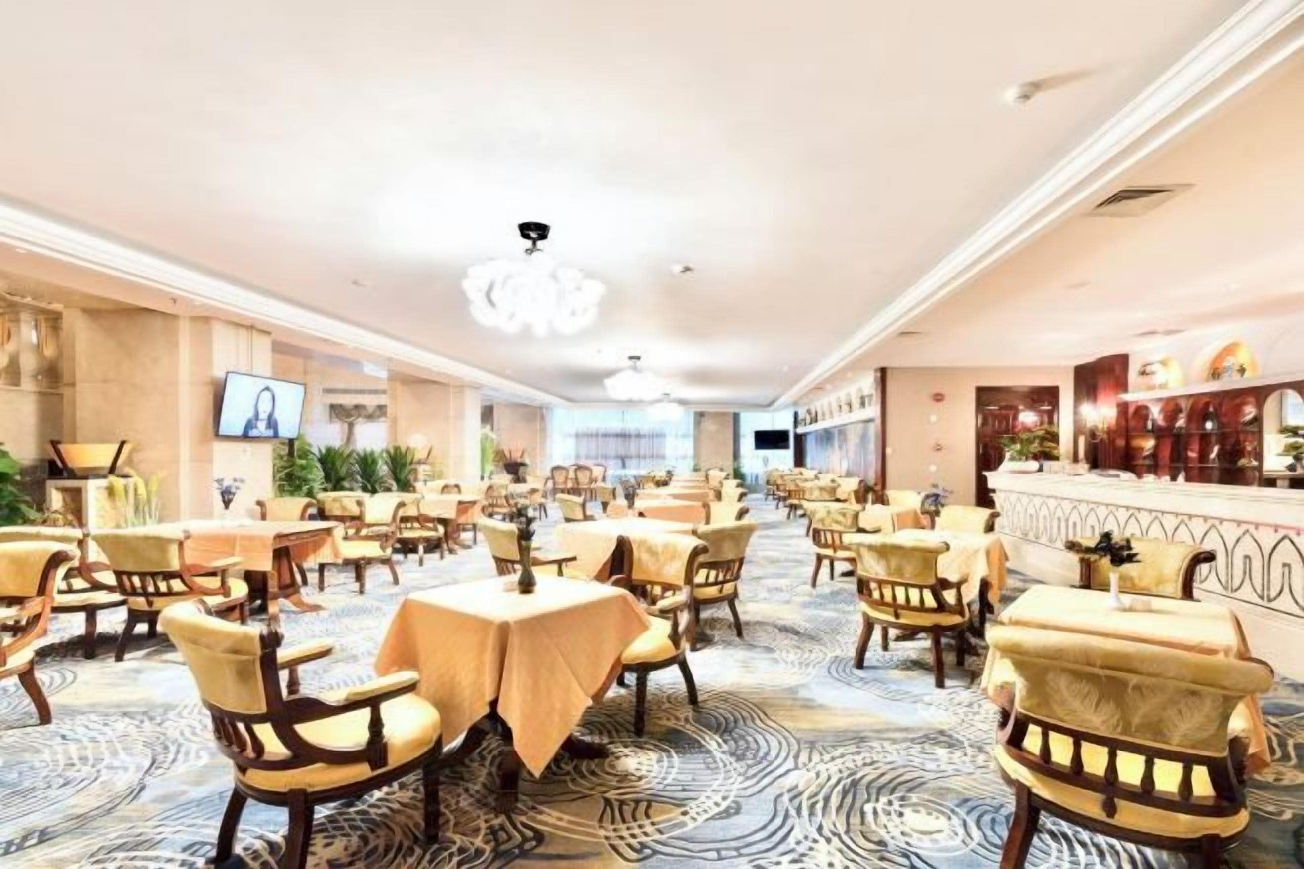 A hotel dining area with multiple tables and chairs, a bar, and a television screen.