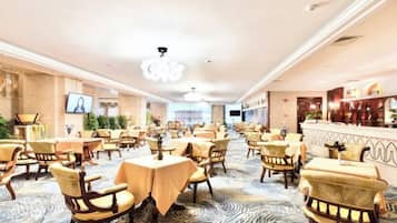A hotel dining area with multiple tables and chairs, a bar, and a television screen.