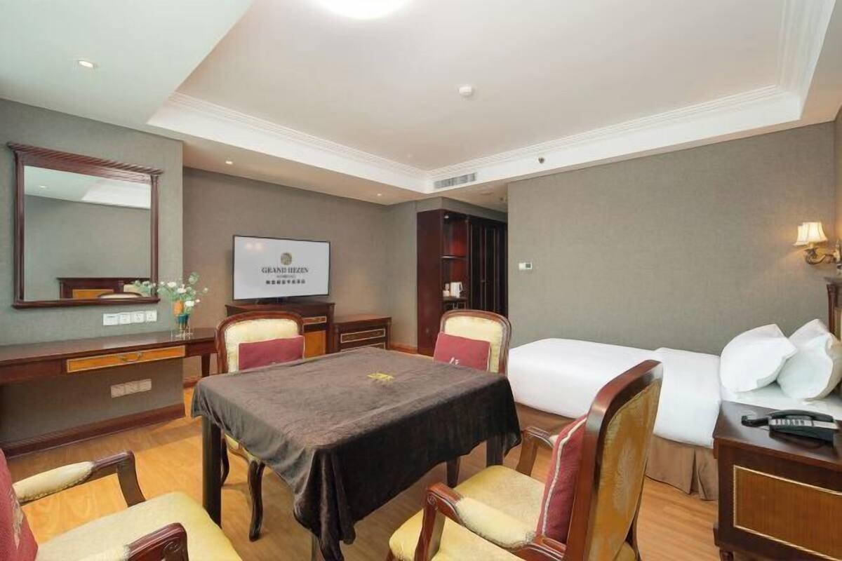 A hotel room with a bed, a desk, a chair, a table, and a television.