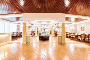 Un hall de hotel espacioso con un mostrador de recepción central, varias zonas de estar y un alto techo con paneles de madera.
