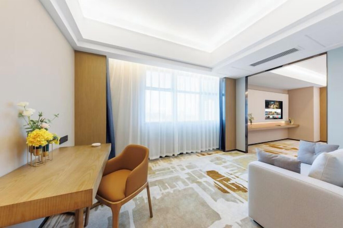 Quarto de hotel com uma mesa de jantar, um sofá, uma TV e uma janela grande com cortinas.