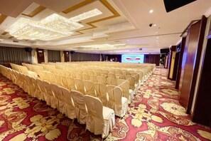 A conference room with rows of chairs covered in white, a red carpet, and a large screen at the front. - Foshan Sanshui ShiHuang Garden Hotel (Foshan)