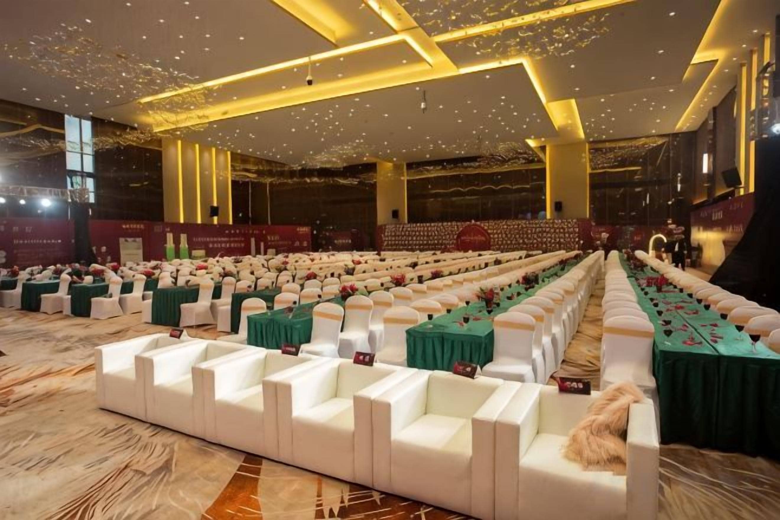 A large hall with rows of white chairs and tables, some with green tablecloths.