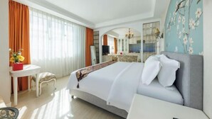 A hotel room with a bed, a desk, a chair, a mirror, and a view of the kitchen. - Foshan Sanshui ShiHuang Garden Hotel (Foshan)