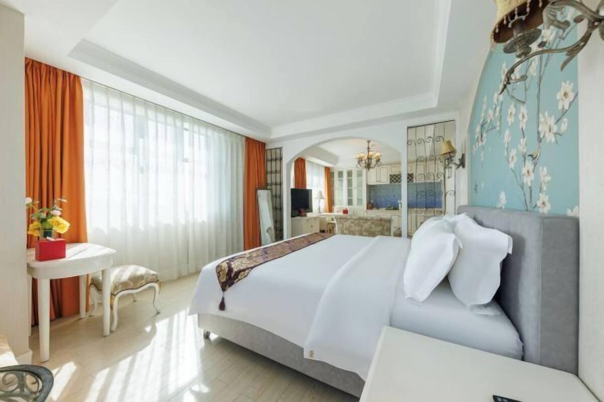 A hotel room with a bed, a desk, a chair, a mirror, and a view of the kitchen.