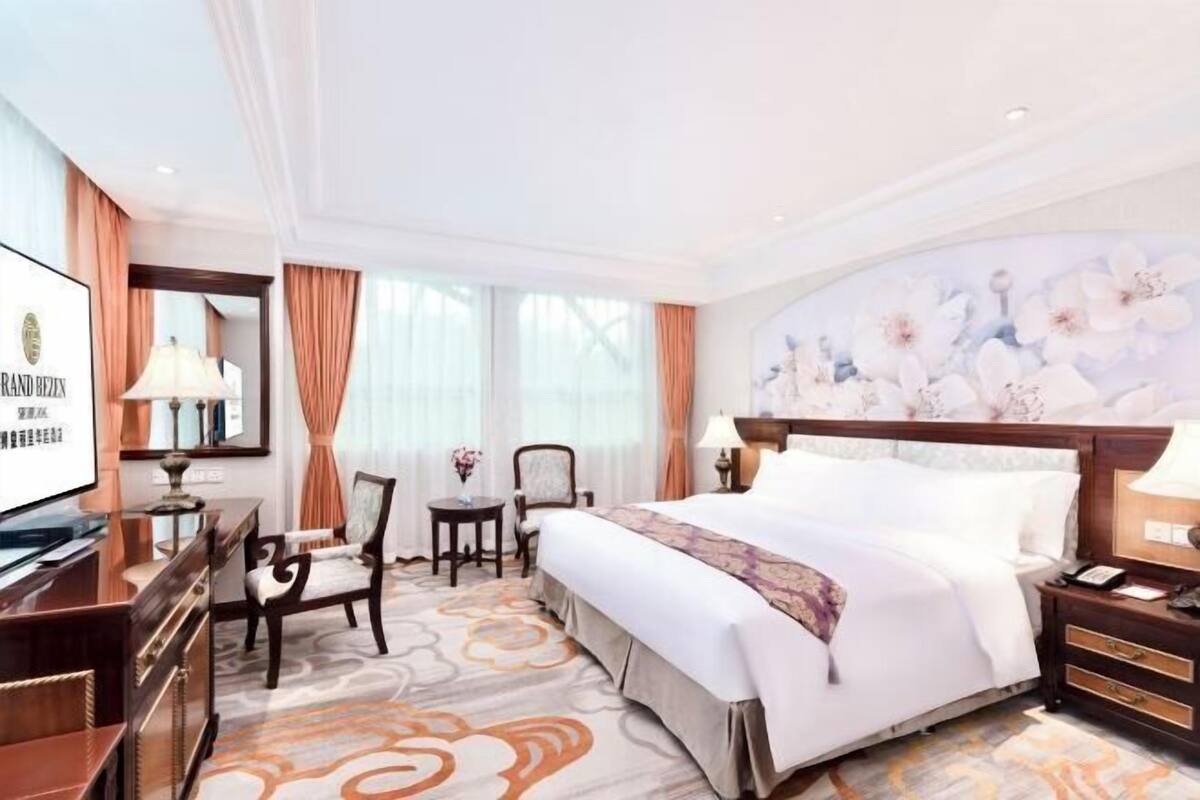A hotel room with a bed, a desk, a chair, a TV, and a large floral wall mural.