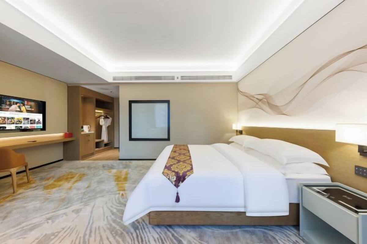 A hotel room with a bed, bedside table, TV, desk, and a mirror.