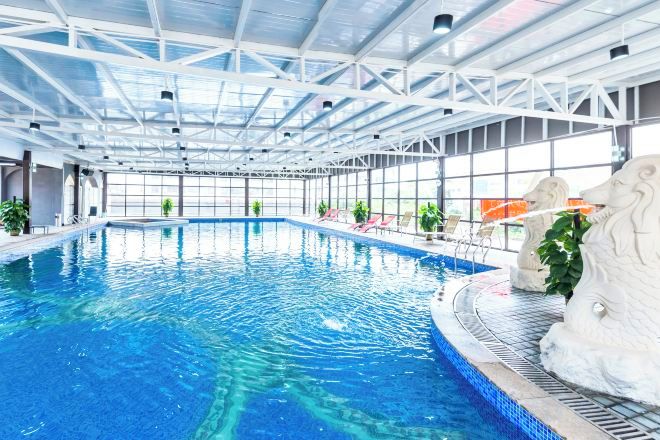 An indoor swimming pool with clear blue water, surrounded by white structural beams and glass walls.
