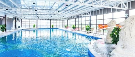 An indoor swimming pool with clear blue water, surrounded by white structural beams and glass walls.