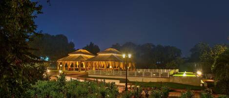 A large, open-air pavilion with multiple seating areas, surrounded by a well-maintained garden with various potted plants.