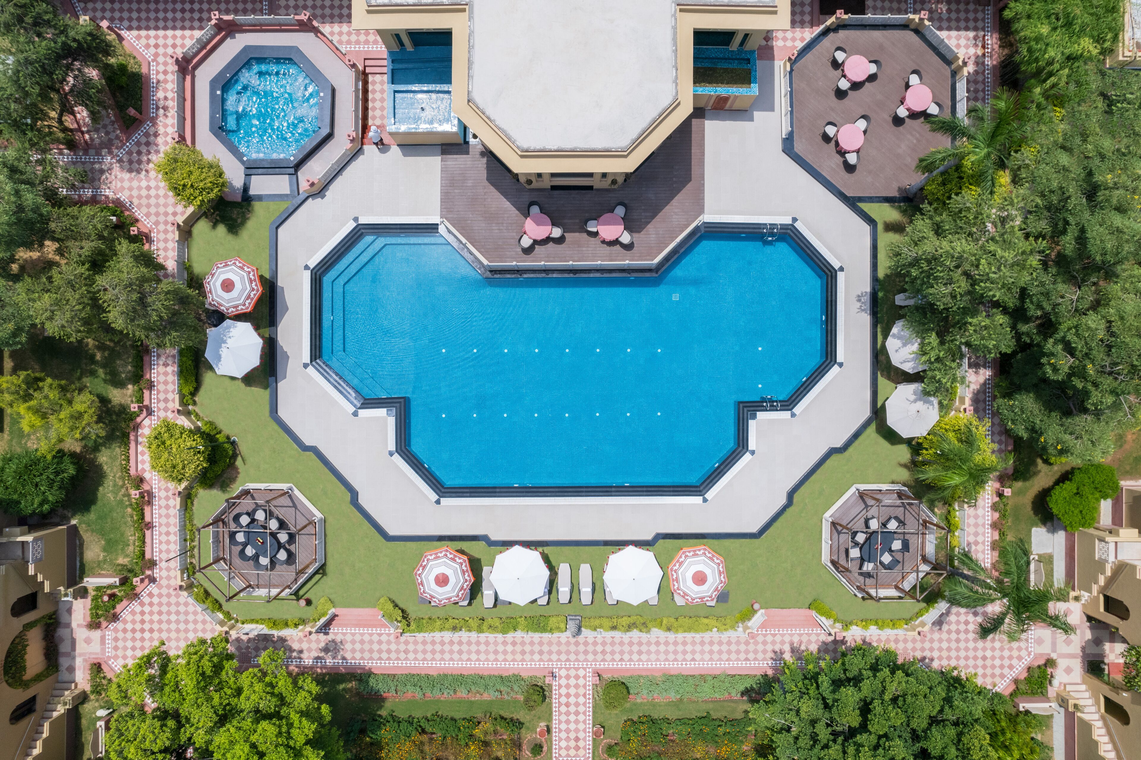 An aerial view of a resort with a central swimming pool, multiple seating areas, and surrounding greenery.