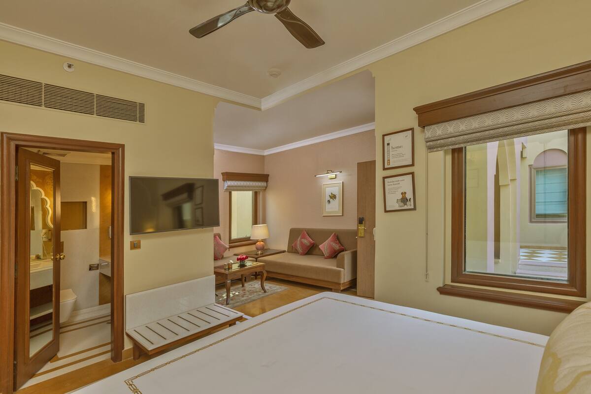 A hotel room with a bed, a sofa, a television, a ceiling fan, and a window.