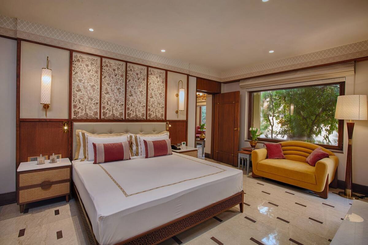 A spacious bedroom with a large bed, a sofa, and a view of greenery outside.