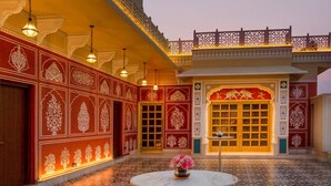 A traditional building with ornate red and white patterns, a tiled courtyard, and a central table with flowers. - Heritage Village Resort & Spa Manesar (Gurugram)